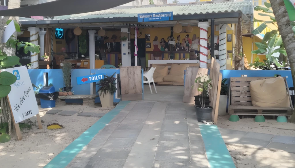The welcoming open-air entrance of Xplorers Restaurant, featuring a tiled walkway, yellow walls with murals, and beach seating.