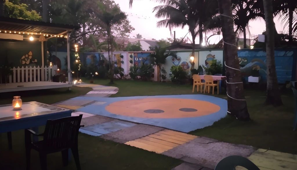 A tranquil view of the colorful garden terrace at twilight, featuring mural-painted walls, string lights, and candlelit tables.